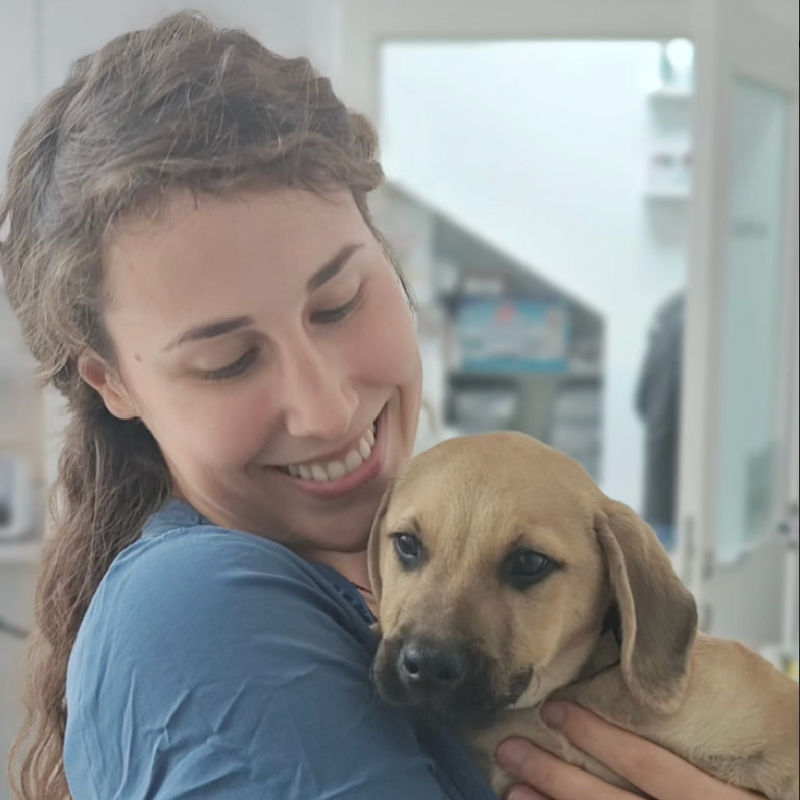 Nataša u plavoj uniformi drži smeđeg šteneta u naručju u veterinarskoj ordinaciji.